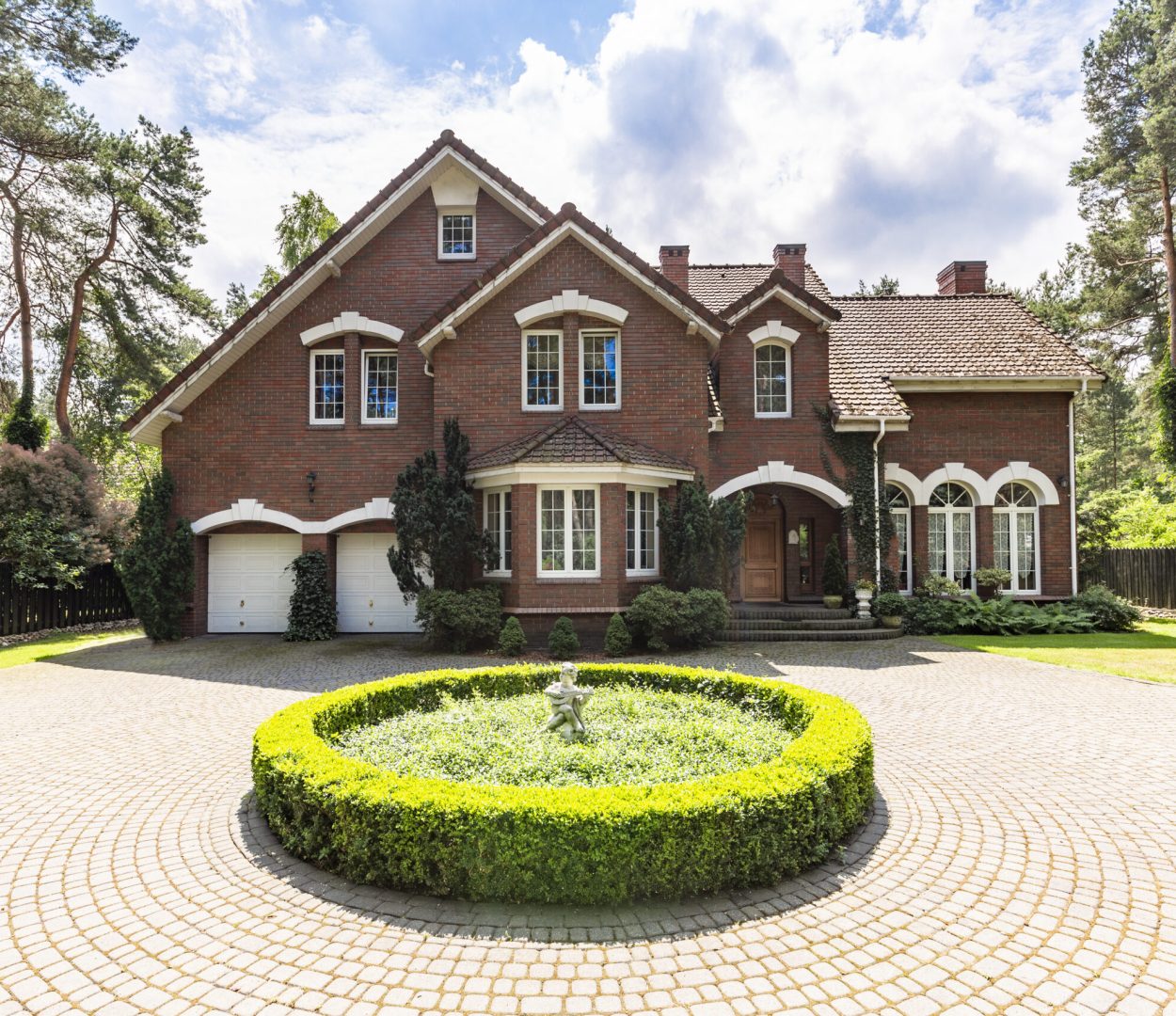 Front view of a driveway with a round garden and big, english style house in the background. Real photo